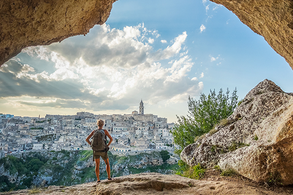 Wide shot from a cave of a backpacker looking out at a city