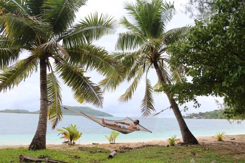 Guy lying down in a hammock that was tied in a palm tree while enjoying the peaceful vibe of the sea