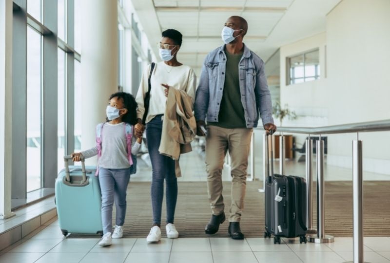 Man, woman and child with suitcases wearing face masks.
