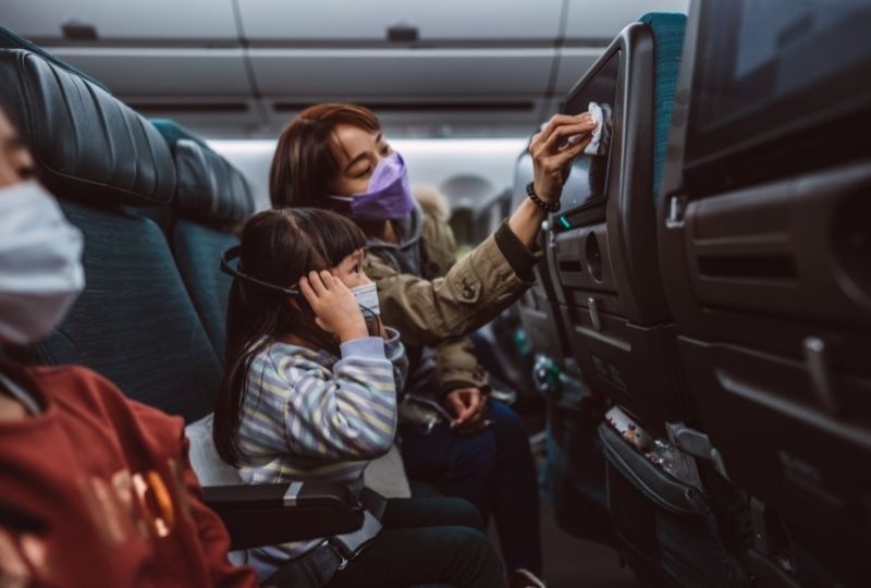 Mother and child wearing masks on an airplane using an antibacterial wipe.
