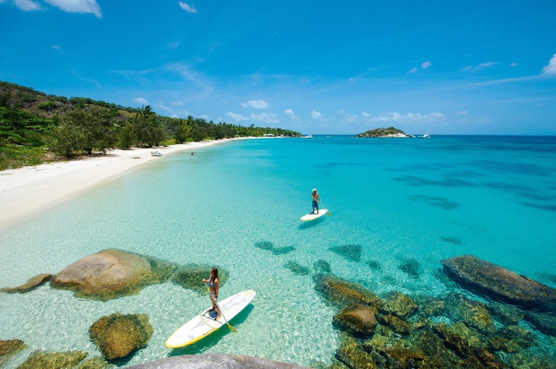 couple stand up paddle boarding over clear waters on lizard island beach qld