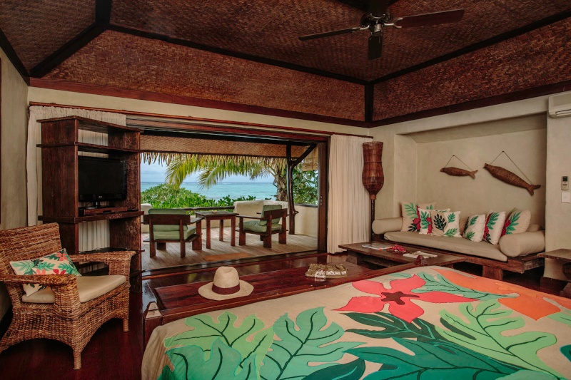 Interior of hotel room looking out to the ocean and tropical garden. There are a lot of wooden features in the room