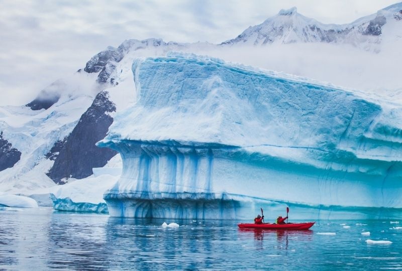 two people are in a bright red kayak with large icebergs behind them