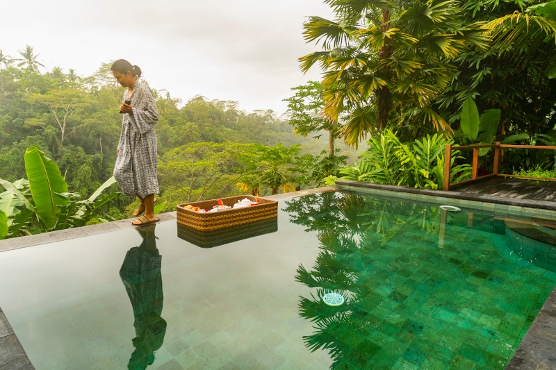 Enjoying Bali, young woman getting ready to soaking steamy pool, and have breakfast at the same time