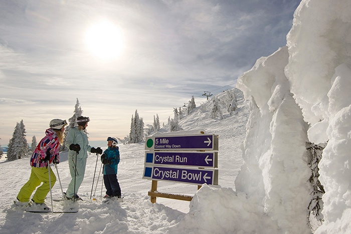 A family in skis standing at directional signs on the ski fields at Sun Peaks Resort 