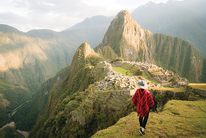 A woman stands in the foreground looking at Machu Picchu and the Inca Trail