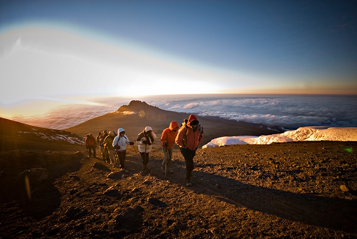 A group of hikers ascend a peak on the Marangu track of Mt Kilimanjaro with the sunrise in the background