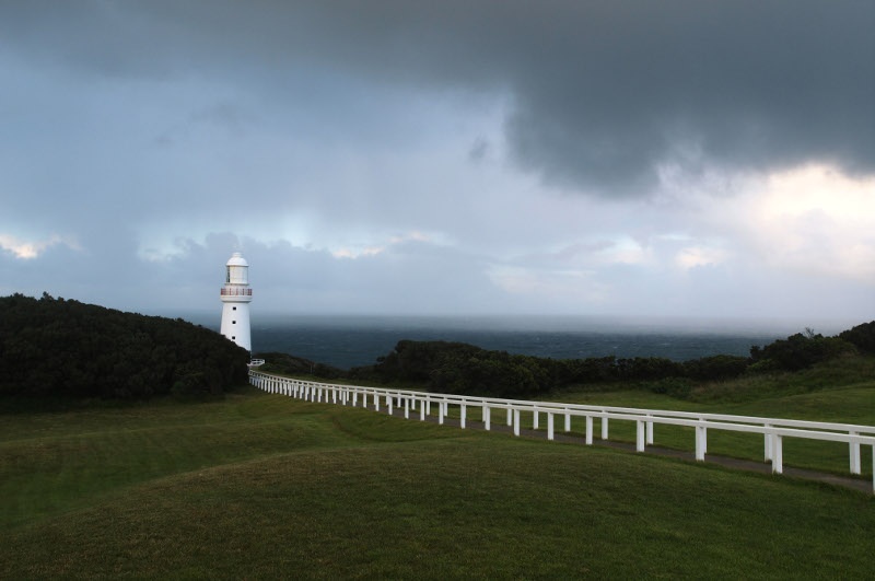 the green meadow lined with white fence and the lighthouse can also be seen from a distance 