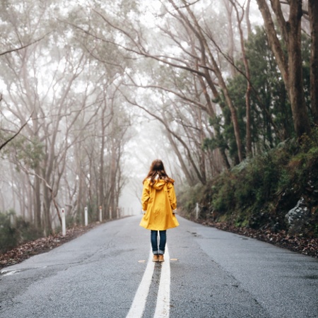 Lady in a bright yellow jacket stands amidst the road in the forest