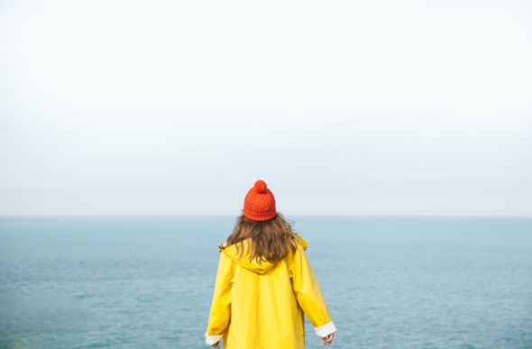 Lady in a bright yellow jacket stands amidst the sea