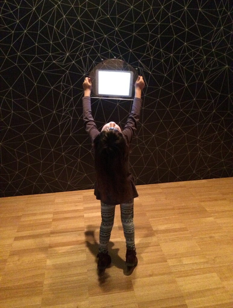  a little kid seems to be looking at a glowing tablet inside the museum