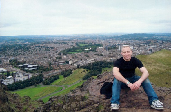 Man sitting on a cliff with a wide view of Edinburgh behind him
