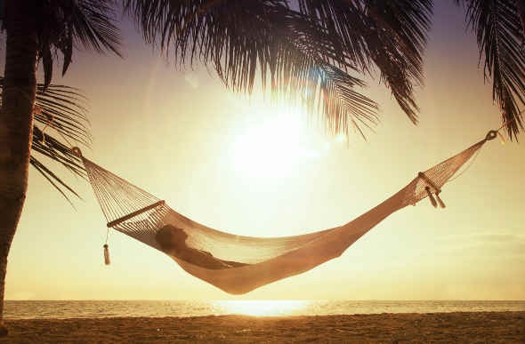  Tourist enjoying the sun while laying down on a hammock tied between two coconut trees