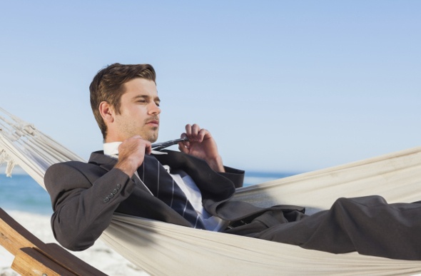  a handsome man on a suite adjusting his neck tie while lying on a white hammock in the beach