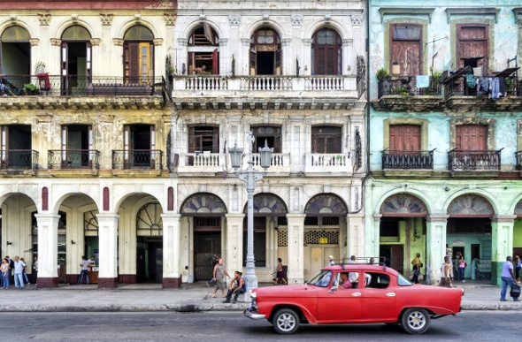  an antique red car parked along the historical buildings in Cuba Havana