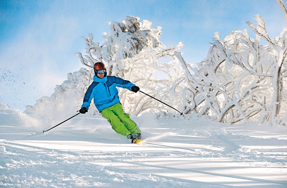  a man in a blue jacket and yellow greent pants skiing in the middle of the snow-filled path
