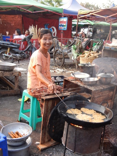  a woman frying street foods on a wok while smiling