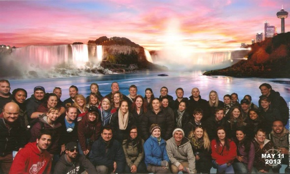 Group of tourists posing for a photo with a sunset over a waterfall in the background