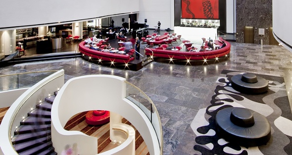  a fancy hotel restaurant with people eating on rounded red couches and waiters serving them