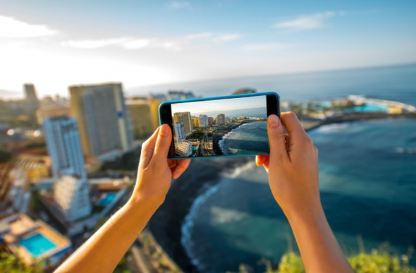  a person holding her phone up to take a picture of the city and beach view from her hotel
