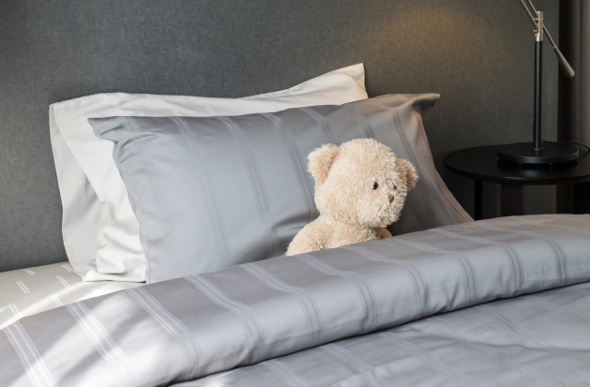  a teddy bear sitting on a king sized bed with white and silver pillow covered in silver beddings 