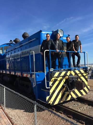 Four men in black standing at the back of a train
