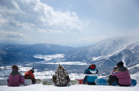 A group of people sitting in the snow looking towards the mountains 