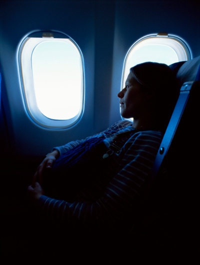 Pregnant woman looks out airplane window while cradling her stomach