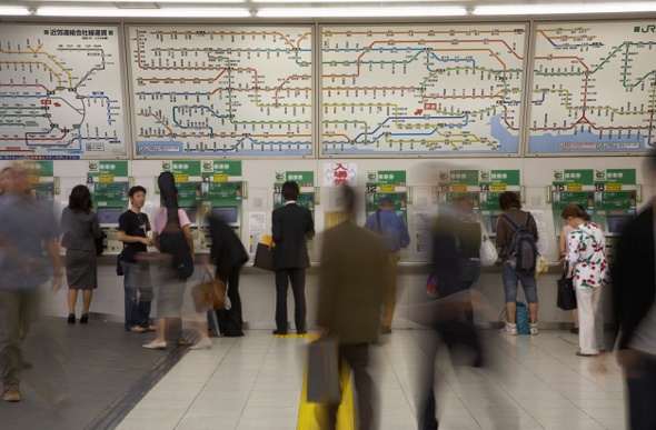  People moving in a busy public transport station in front of a colour-coded map
