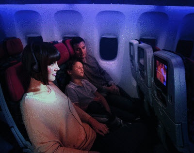  the mother watching movies on the small screen while her husband and son is sleeping on the VA economy class plane
