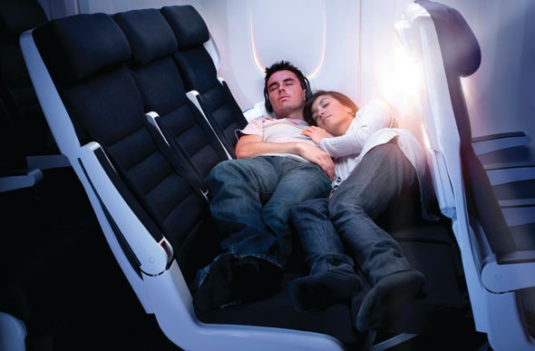  a couple sleeping on the very spacious black and white seats of the air new zealand economy 