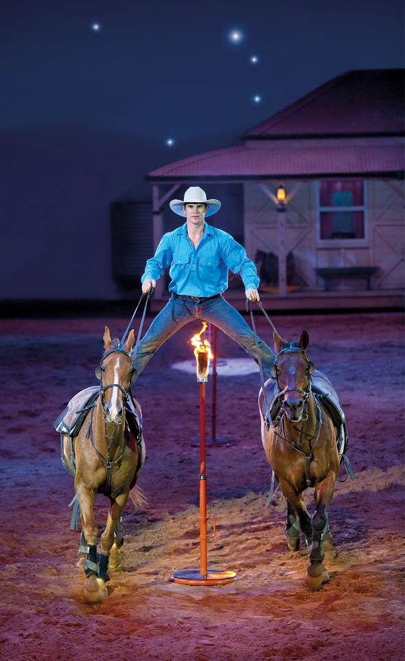  A guy riding 2 horses while crossing a post with fire