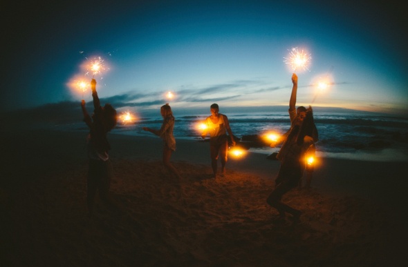  friends happily lighting firework sparklers on the beach at night