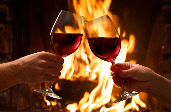 Two wine glasses held in front of a fireplace