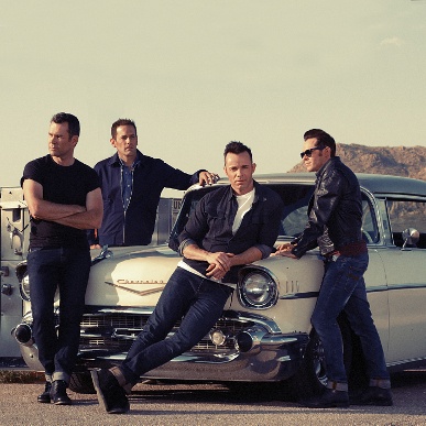 Four men in black posing in front of a white vintage car