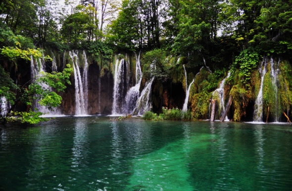  Waterfalls flowing past vegetation into green water 