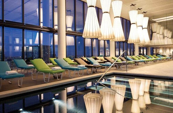  blue and green lounge chairs on the side of an indoor pool adorned with fancy hanging lights