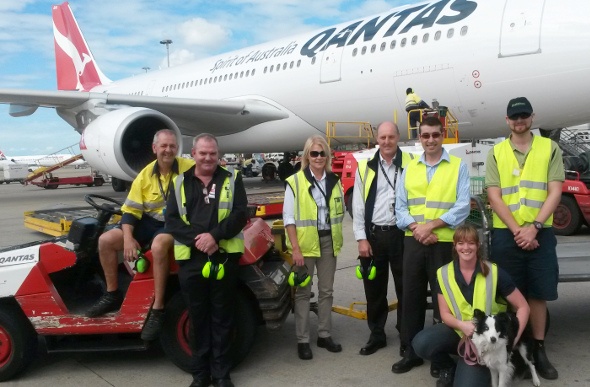  airport workers and a dog in front of a QANTAS plane 