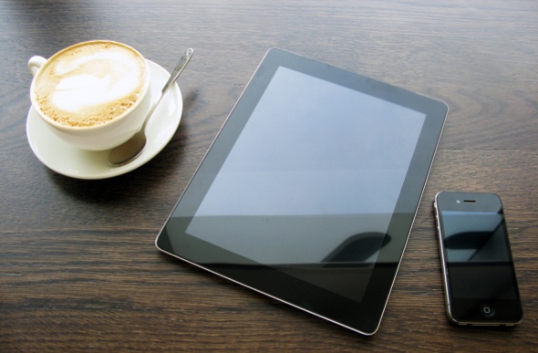 A tablet and a smartphone on the table with a cup of hot coffee