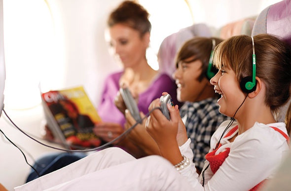  the kids playing on the small LED TV on the airplane while their mom is reading a magazine
