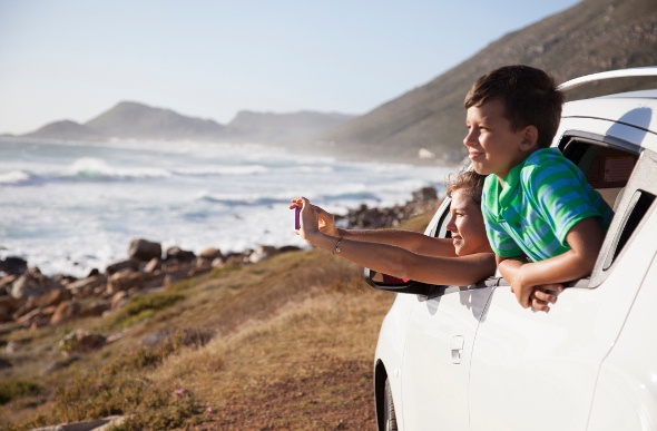 Two kids looking out the window of their car at a beach view