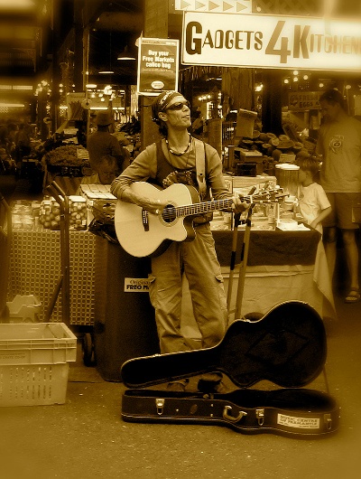  a busker playing his guitar in front a market