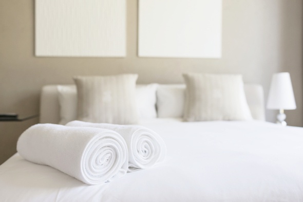 rolled white hotel towels placed on top of a white king-sized bed