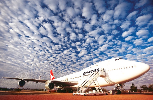Full shot of a Qantas airplane under the patchy clouds