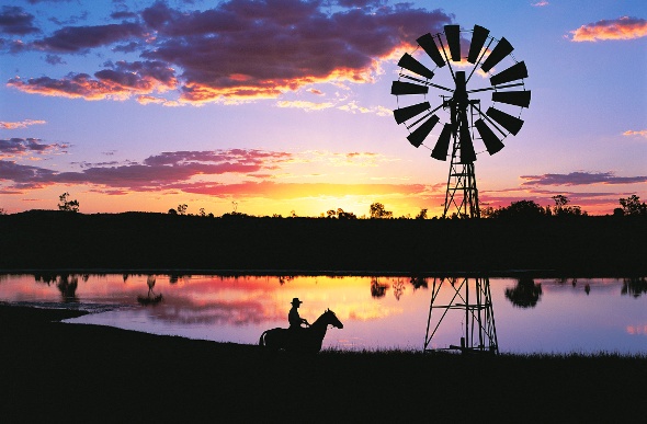 Silhouette of a windmill and a cowboy riding his horse as the sun sets across the lake