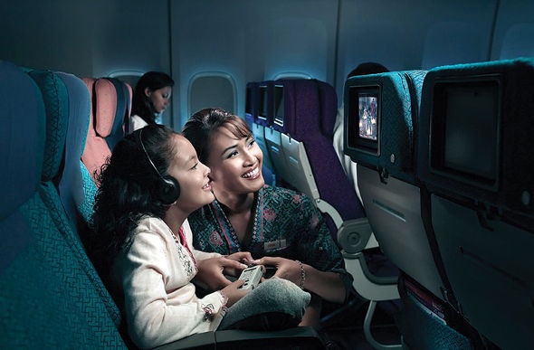  A malaysia Airline flight attendant assisting a curly liitle girl who wants to watch on the led screen at the back of the seat in front of her