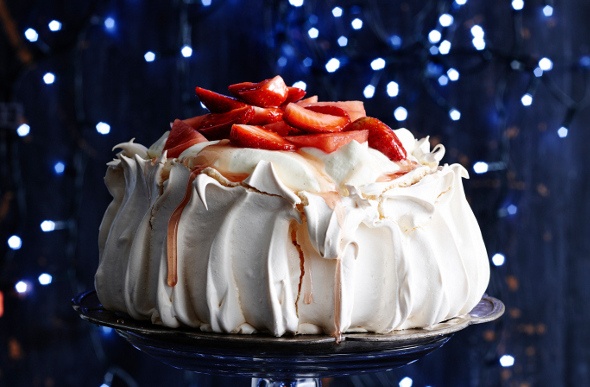 Large, strawberry-topped pavlova on a plate surrounded by small blue lights