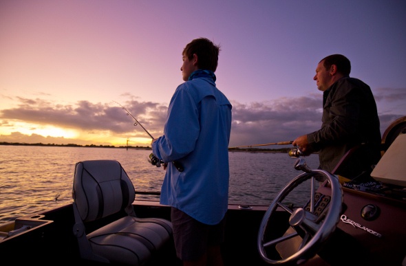 Two men fishing on a boat as the sun sets