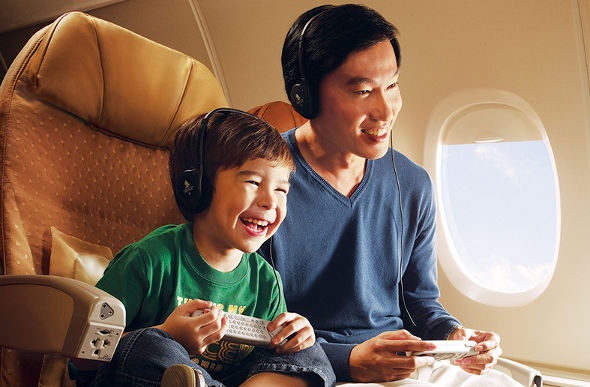  an asian dad and his son happily playing videogames together on the console available in the singapore airlines plane