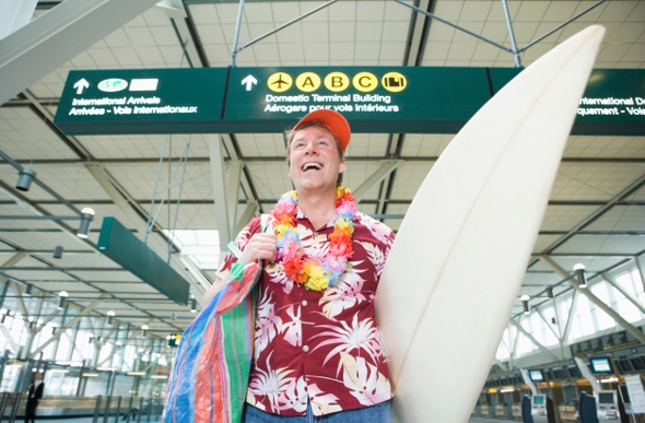  Excited traveller at the airport wearing a lei and holding a surf board 